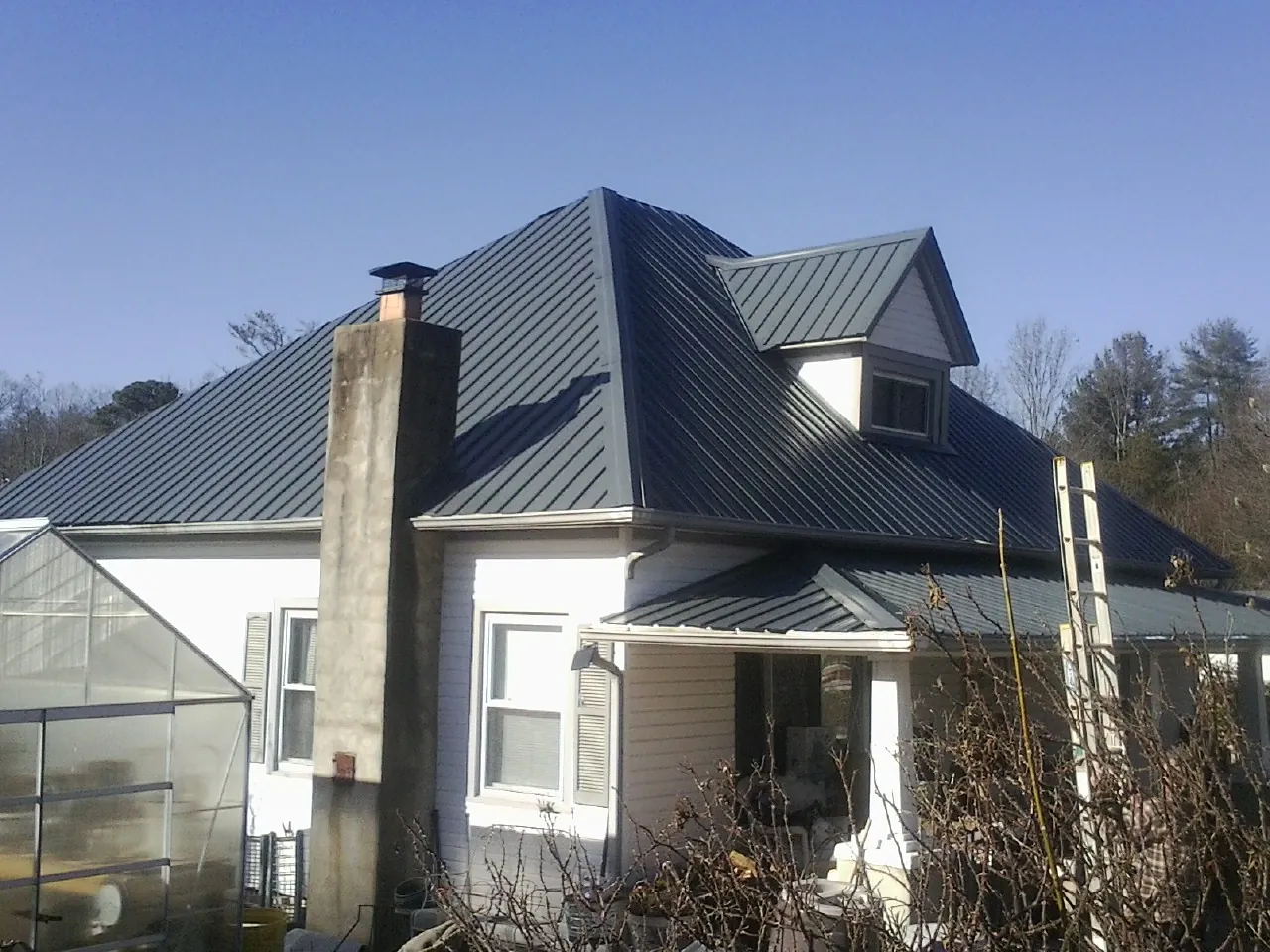 Dark blue standing seam metal roof on a white farmhouse with dormer — Slate & Tile Roof Repair by Roofing Brothers in Fertile