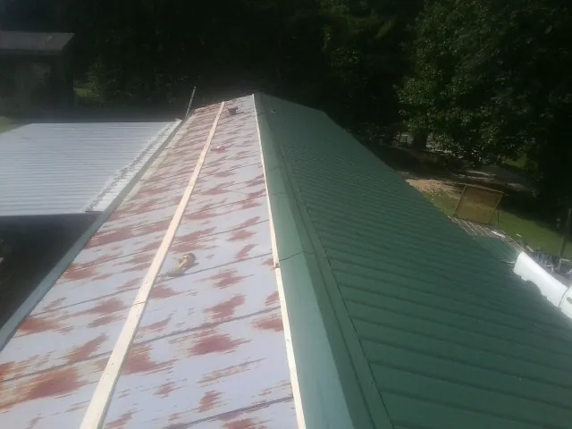 Old rusted panels beside newly installed green metal roofing — Wind Damage Roof Repair by Roofing Brothers in Fertile