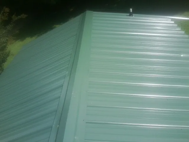 New green metal panels meeting at the ridge of a roof — Flat Roof Repair work by our crew in Fertile