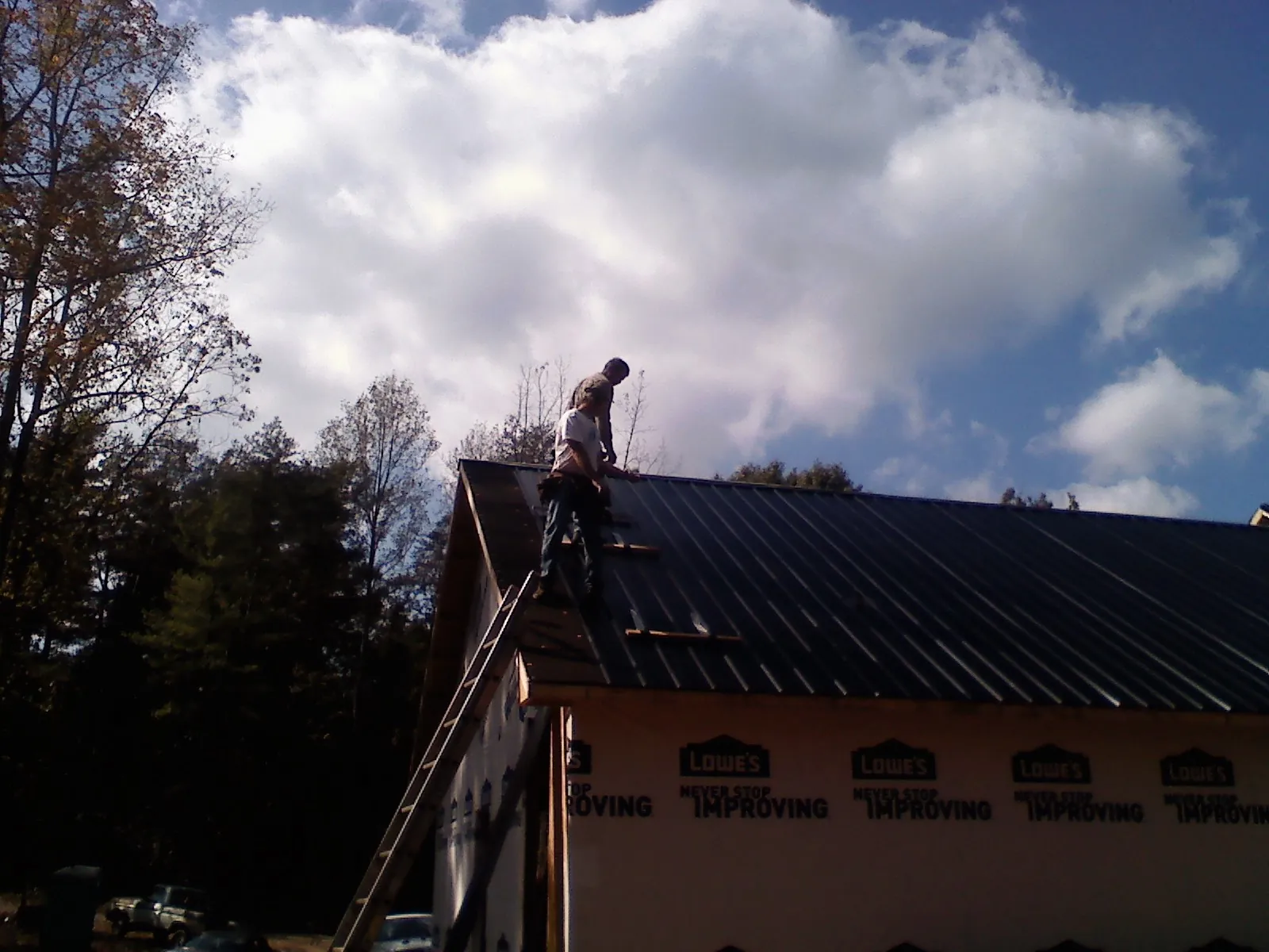 Roofer fastening dark metal panels high against a cloudy sky, from a Roof Inspection job in Fertile
