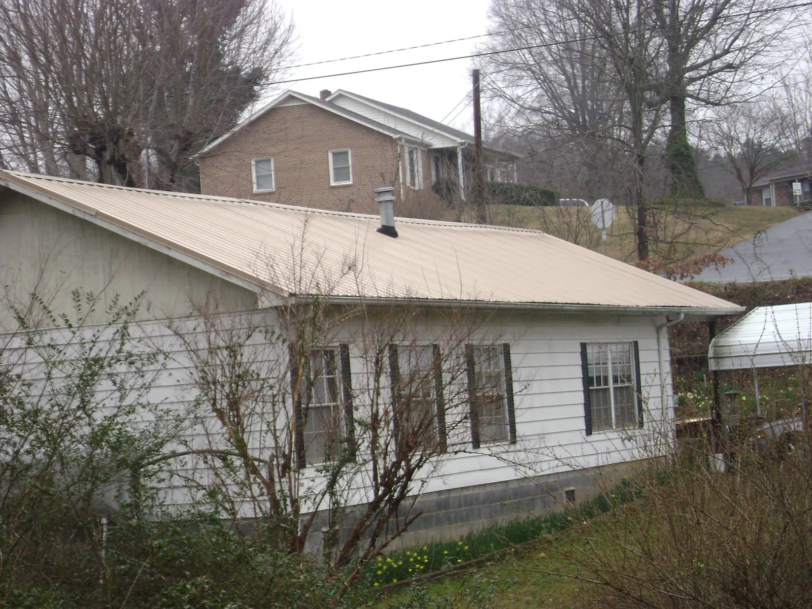 Tan metal roof on a white sided house set into a hillside — Commercial Roofing by Roofing Brothers in Fertile