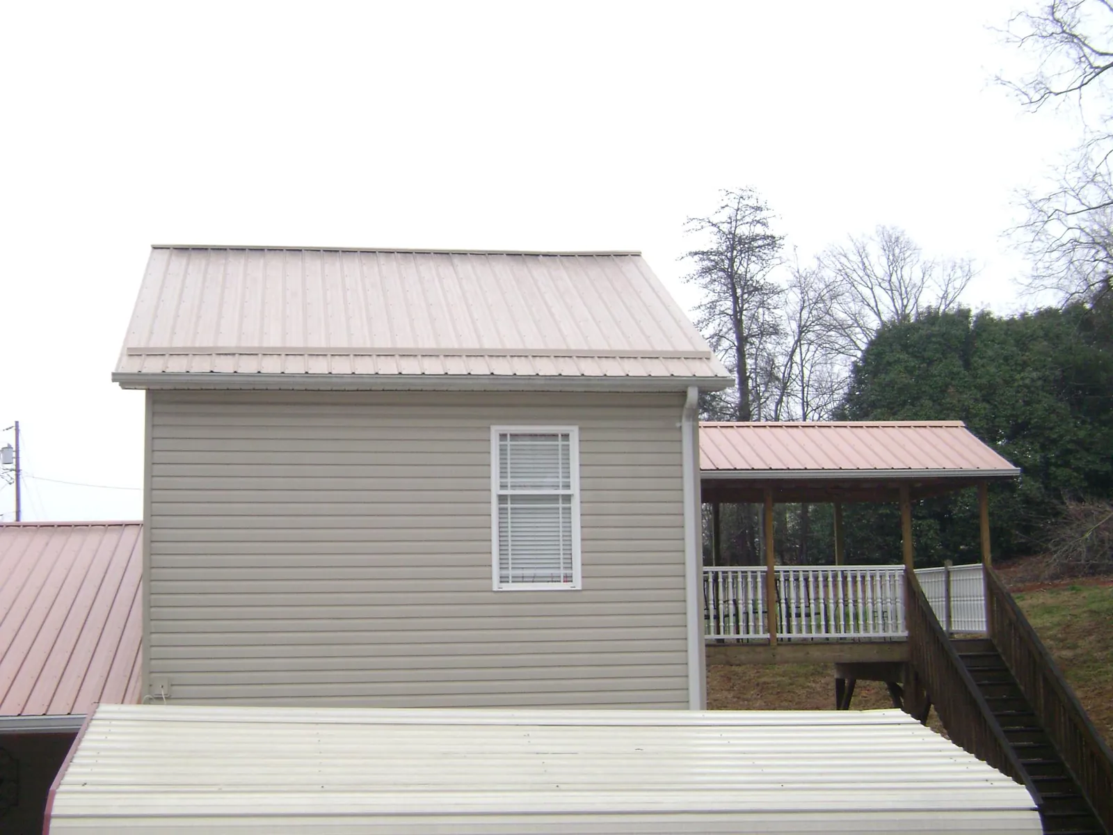 Tan metal roofs on a two story addition and attached porch, from a Roof Replacement job in Fertile